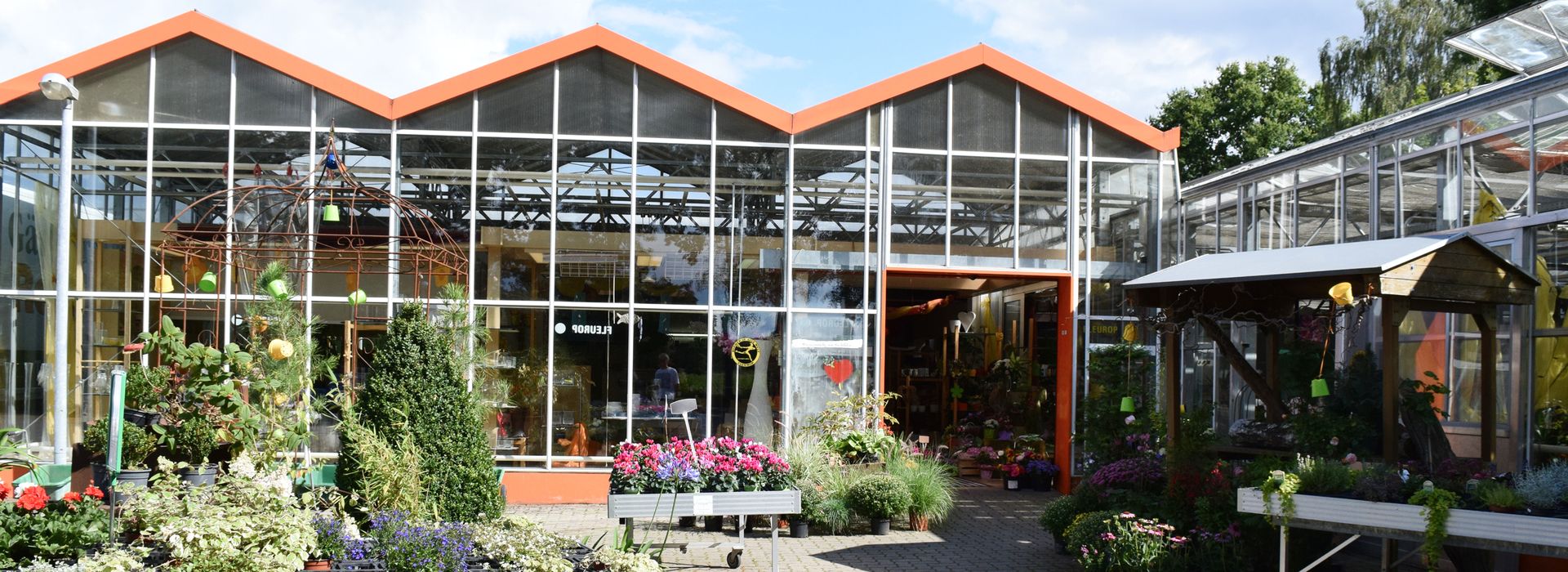 Außenansicht der Gärtnerei Reinike mit bunten Blumen und Gewächshaus.